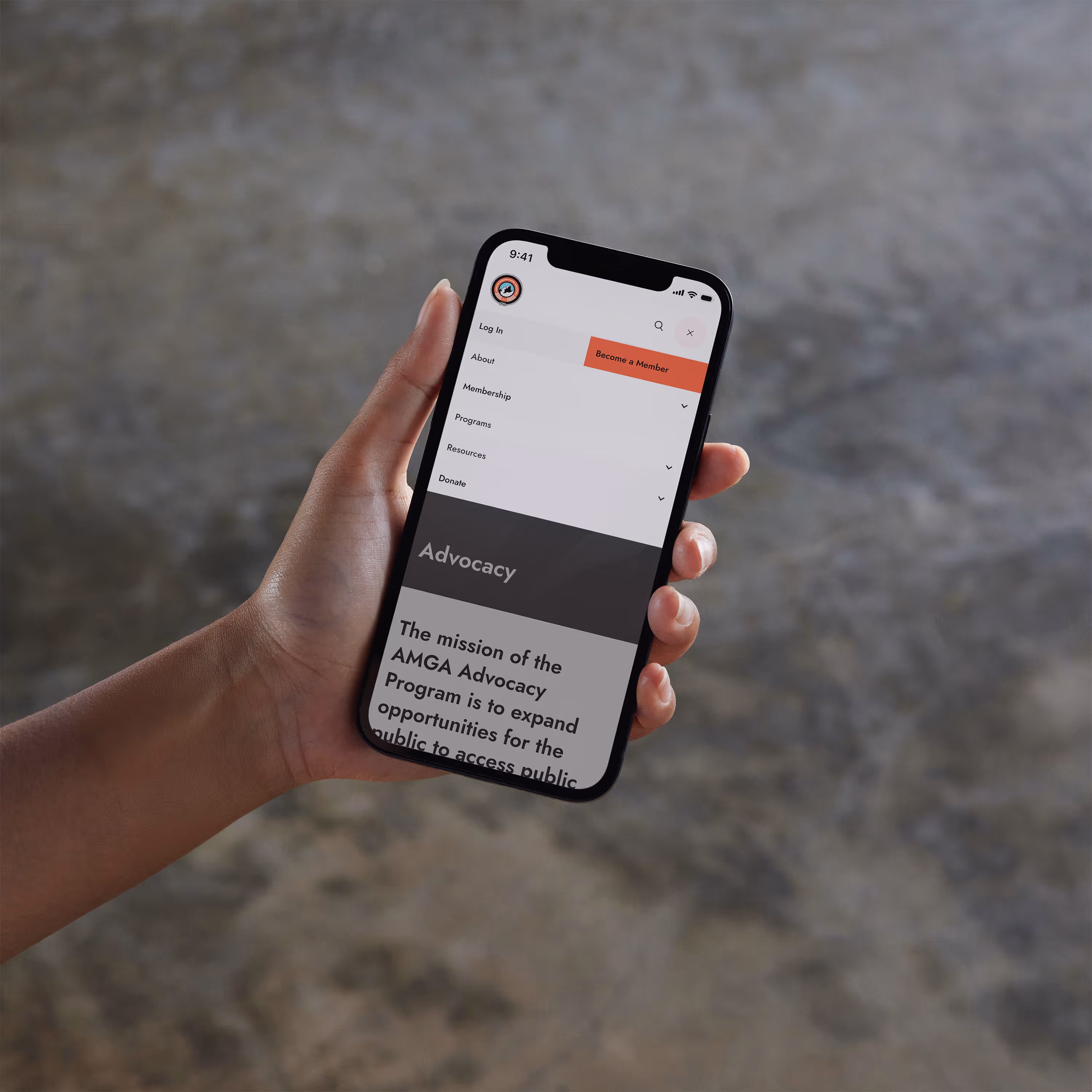 A person's arm holding a smart phone with the AMGA's mobile website's global navigation open.