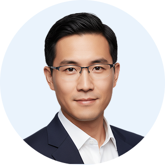 Headshot of a man with black hair wearing rectangular glasses, a white shirt, and a dark blazer, against a light background.