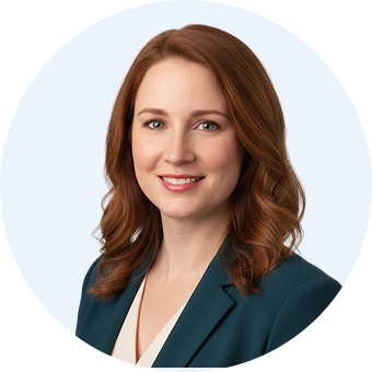 Smiling woman with shoulder-length auburn hair wearing a teal blazer and white blouse against a light blue circular background.