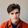 Portrait of a young man with dark hair wearing an orange jacket.