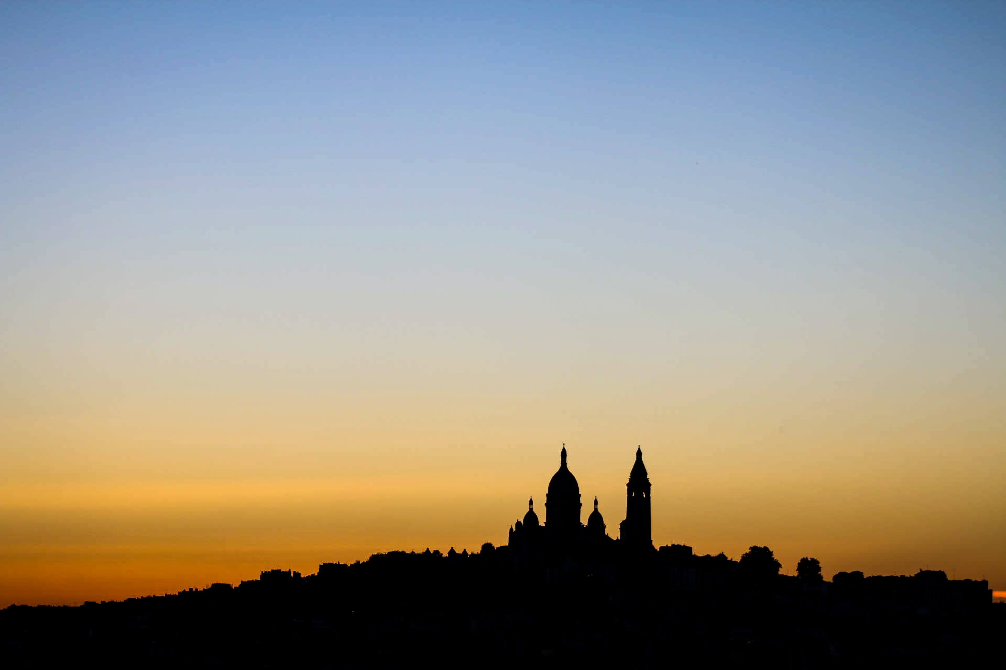 Silhouette of a city skyline with domes and towers against a gradient sunset sky.