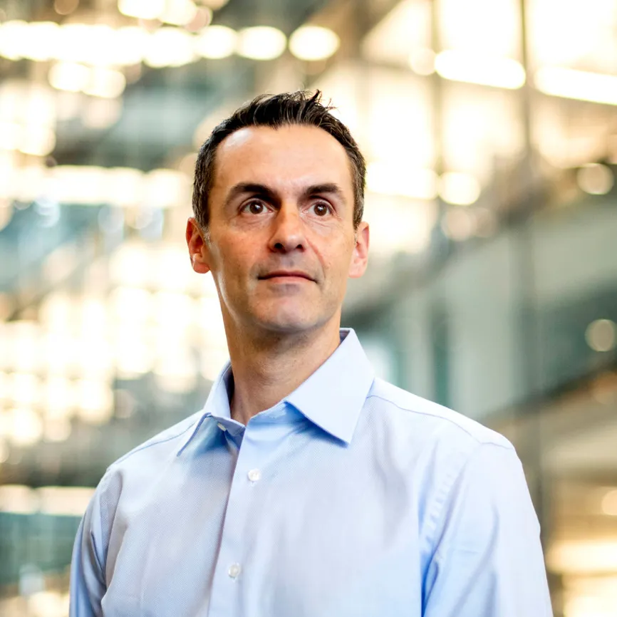 Dr. Grayson Kimball, CMPC, portrait of a man in a light blue dress shirt looking to the side in an office with glass walls and bright lighting.