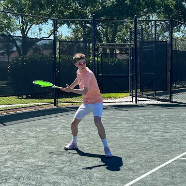 johny mathes, a young man in pink shirt and white shorts preparing to hit a tennis ball on an outdoor court.