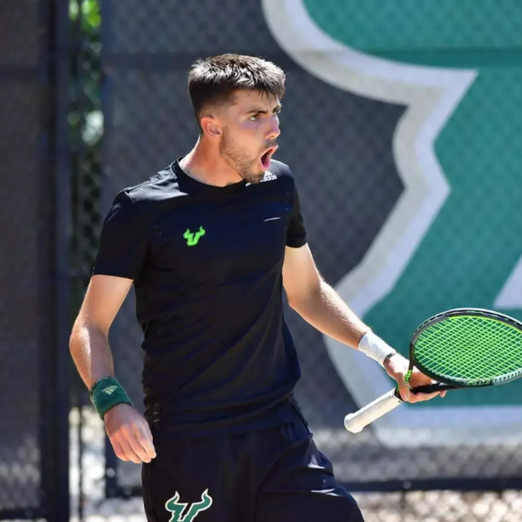 antonio muniz, a male tennis player in black outfit holding a tennis racket with green strings, expressing intense emotion on the court.