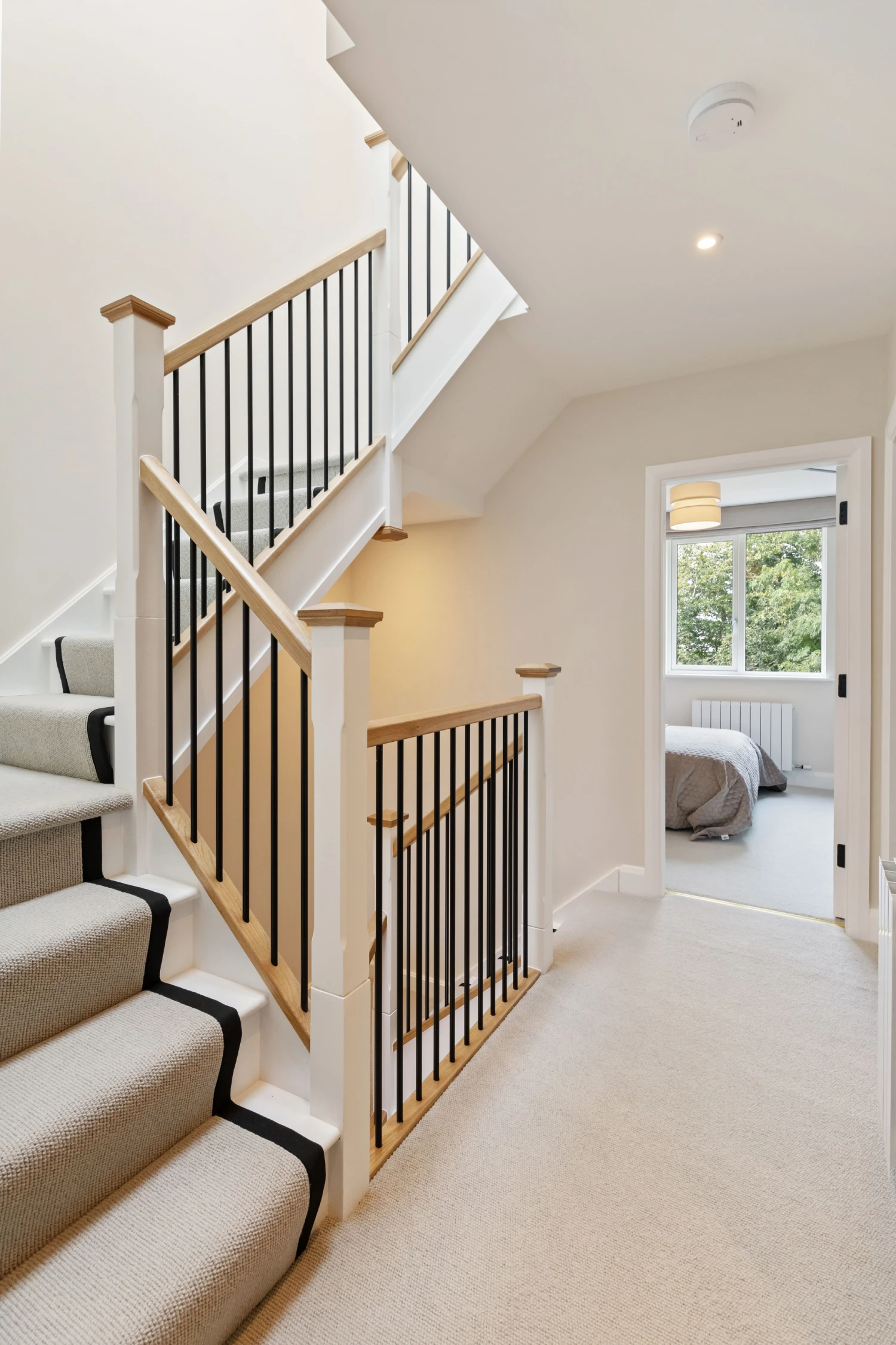 Carpeted staircase with black metal balusters and wooden handrails leading to a hallway with beige carpet and a bedroom visible through an open door.