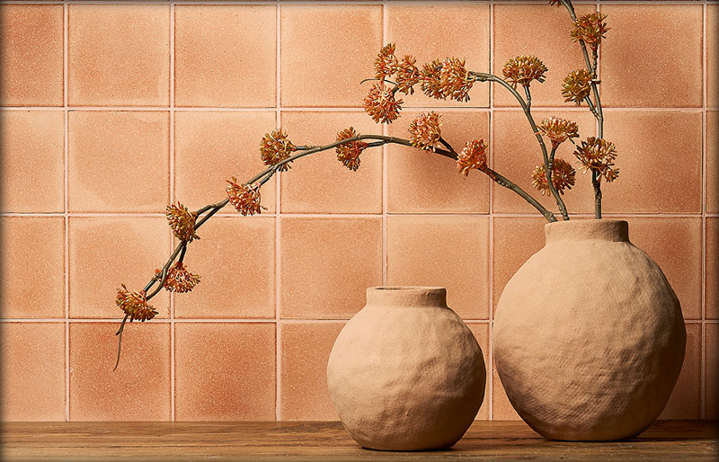 A wall decorated with orange sustainable Eralith tiles, with ceramics and dried flowers in front of it.