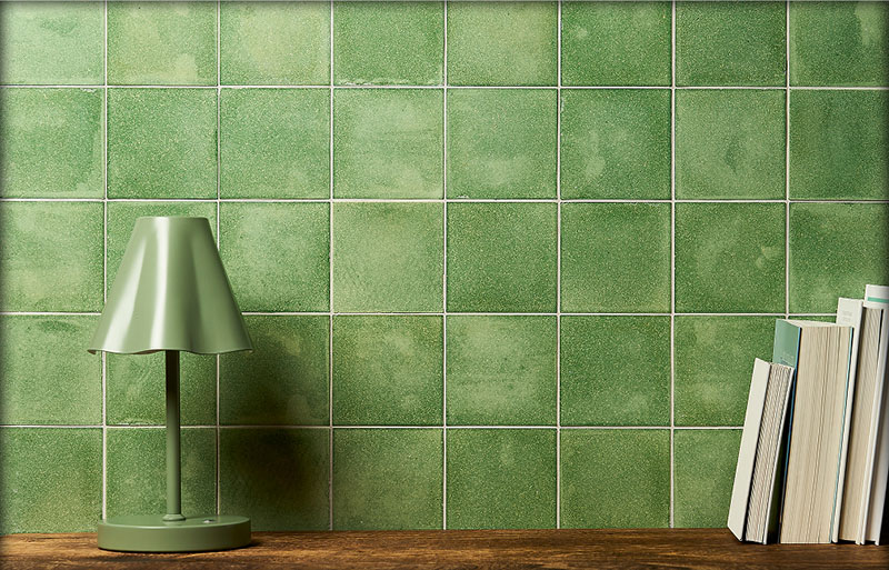 An internal wall tiled with green sustainable Eralith tiles, with a vase and reading books in the foreground. 