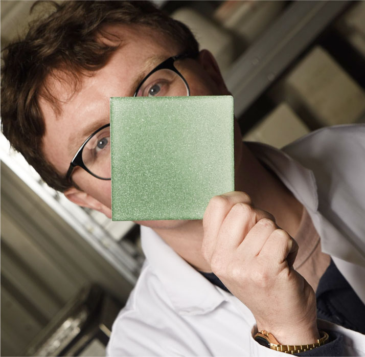 Dekiln CEO, Dr Aled Roberts displaying a light green sustainable Eralith tile, holding it up to his face. 