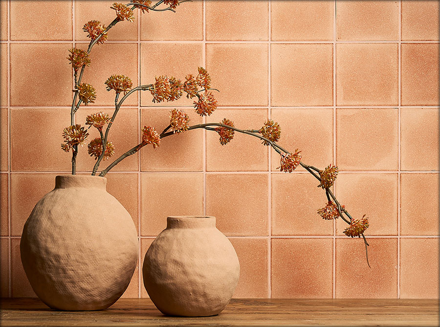 A light-organge Eralith tiled wall, with two ceramic pots and dried flowers in the foreground. 