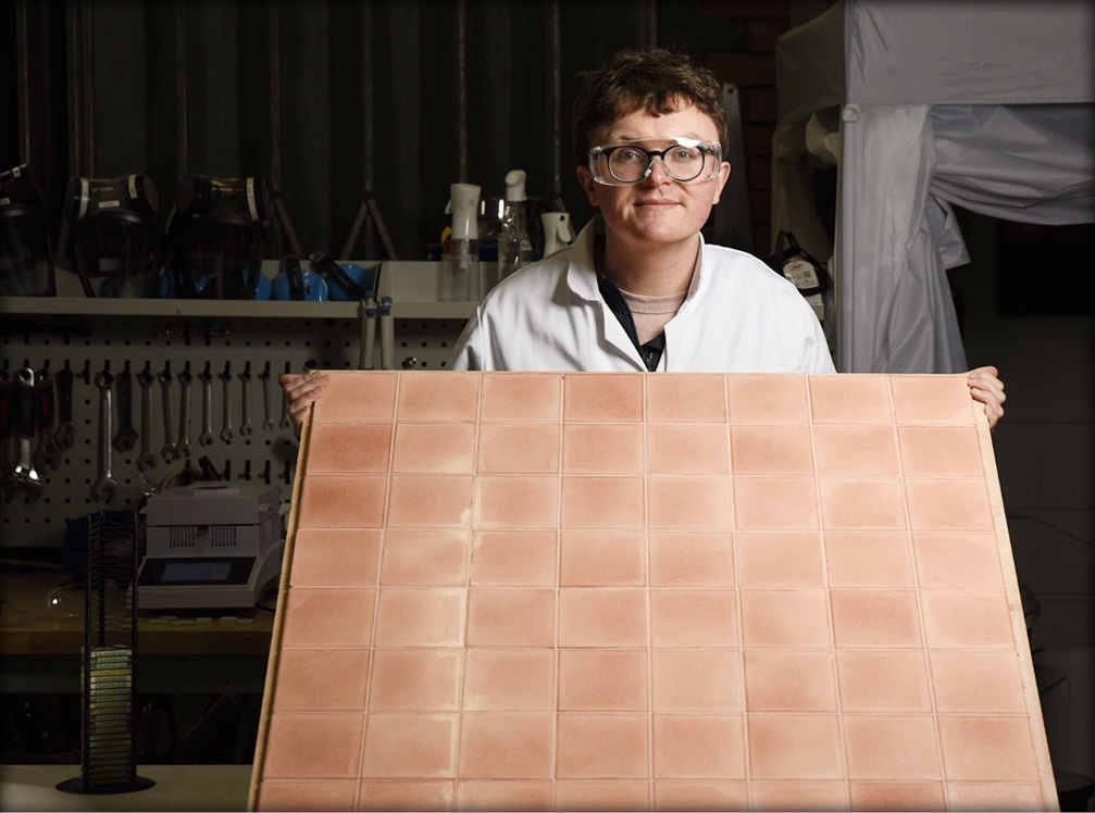 CEO Dr Aled Roberts displaying a large compilation of light-orange sustainable Eralith tiles. 
