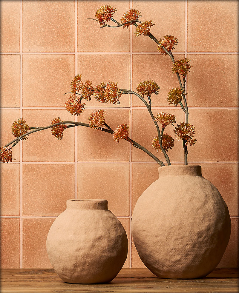 An orange Eralith-tiled wall with two ceramic pots and dried flowers. 
