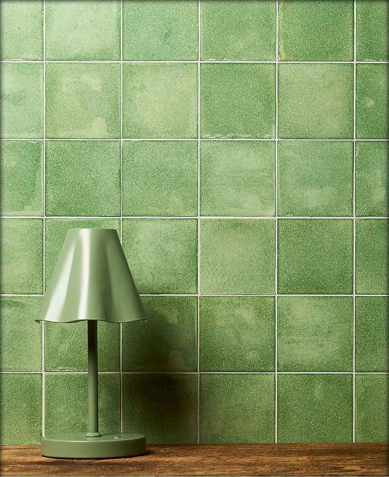 An internal wall tiled with green sustainable Eralith tiles, with a vase and reading books in the foreground.