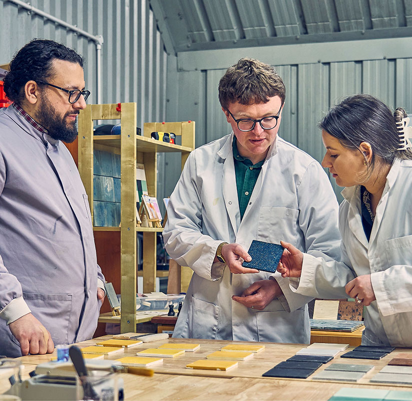 Dekiln team members, including CEO Dr Aled Roberts and Senior Engineer Dr Periklis Petropoulos discussing and examining a blue Eralith tile in a laboratory.