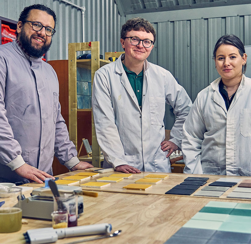 Dekiln team members, including CEO Dr Aled Roberts and Senior Engineer Dr Periklis Petropoulos smiling in a laboratory, standing next to a display of Eralith tiles. 