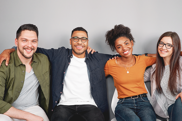 Four diverse church donors smiling, seated closely with arms around each other against a gray background.
