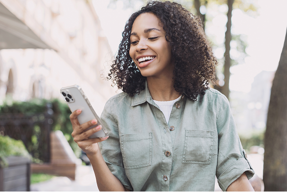 Smiling female Giving in Faith survey respondent with curly hair looking at her smartphone outdoors on a sunny day.