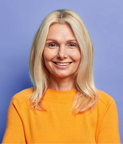 Smiling middle-aged woman with blonde hair wearing an orange sweater against a blue background.