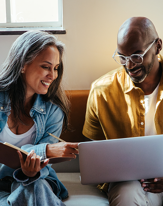 Church leaders smiling while working together on a laptop and notebook in a casual setting.