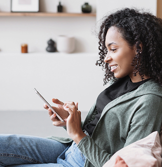 Smiling female church donor with curly hair using a digital giving tool on her mobile phone while seated indoors on a couch.