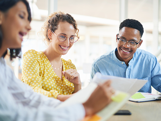 A small group of researchers, academics, and journalists smiling and discussing the Giving in Faith report methodology around a table in a bright office.