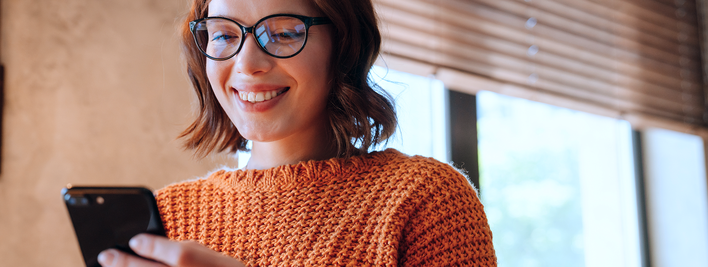 Female church donor wearing glasses and an orange sweater using a mobile phone to give to her church.