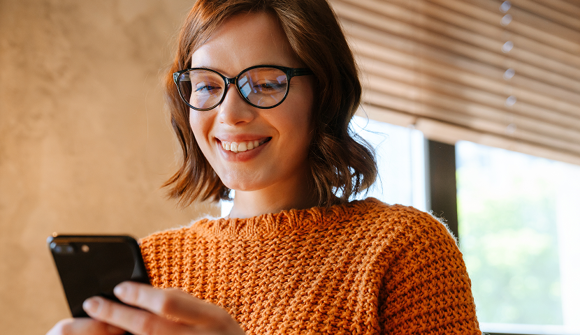Female church donor wearing glasses and an orange sweater using a mobile phone to give to her church.
