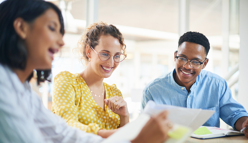 A small group of researchers, academics, and journalists smiling and discussing the Giving in Faith report methodology around a table in a bright office.