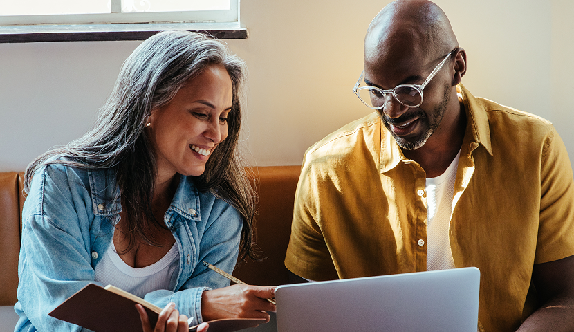 Church leaders smiling while working together on a laptop and notebook in a casual setting.