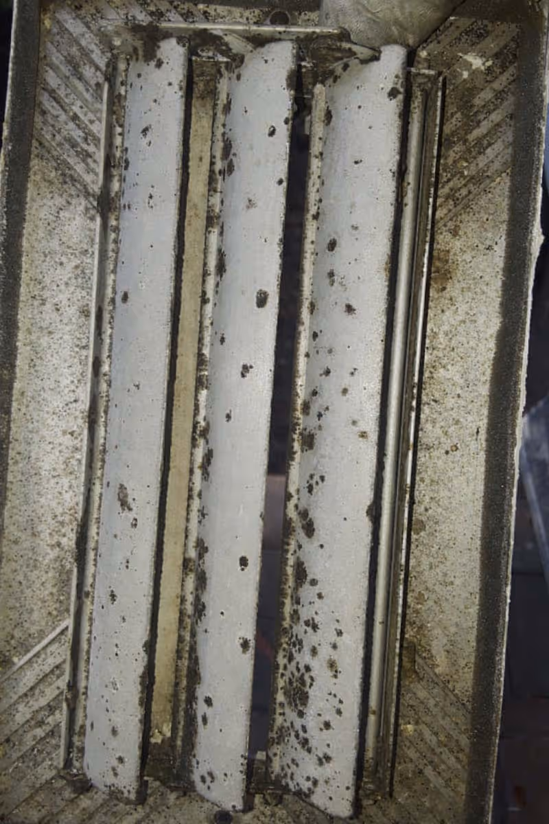 Close-up of white air vent covers with numerous black mold spots and dirt on and around the slats.