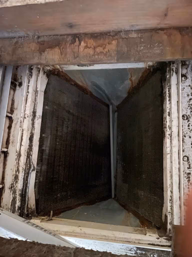 Dirty and rusty air conditioning vent with visible mold and corrosion on metal and wood components.