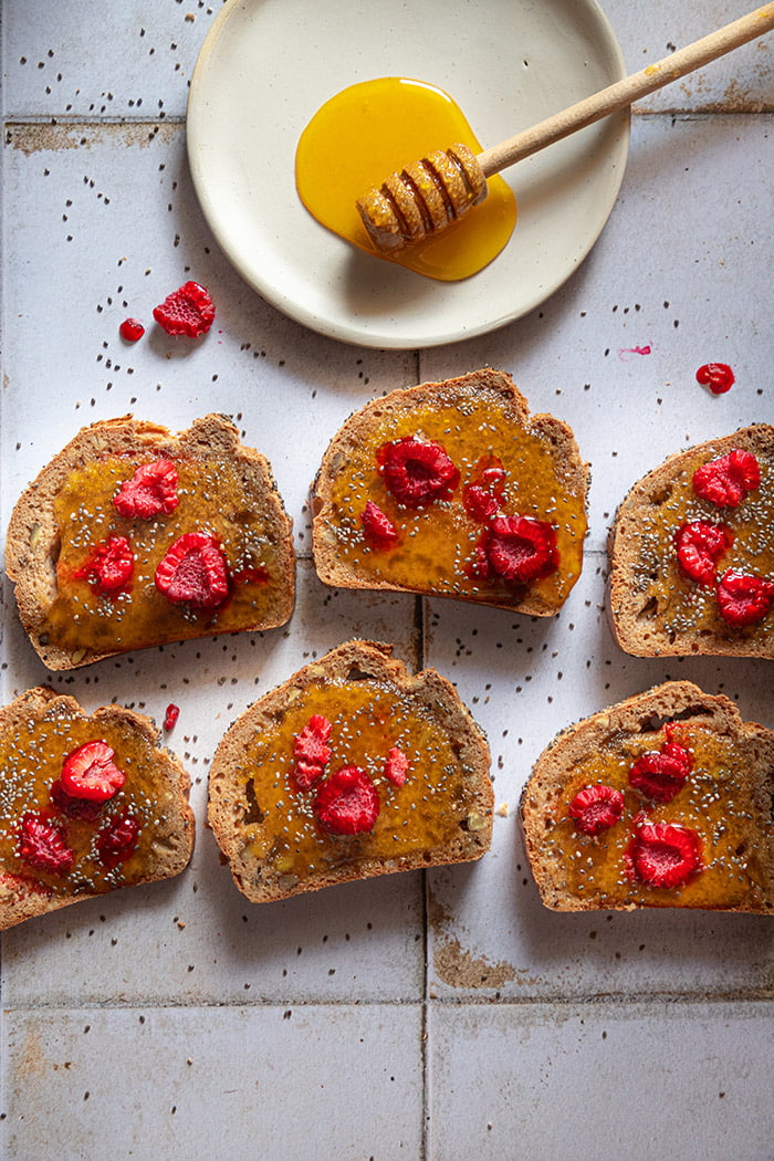 Raspberries on bread and honey on a white plate