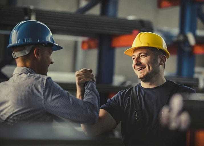 Two industrial warehouse managers in hard hats shaking hands, representing a successful 3PL partnership and reliable logistics management.