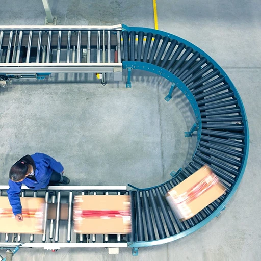 Top-down view of a curved warehouse conveyor belt with a worker monitoring the automated flow of goods in a BASIC 3PL robotic facility.