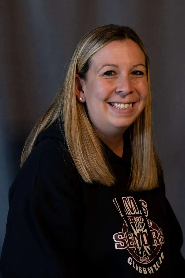 M Smith staff member smiling in school seniors sweatshirt