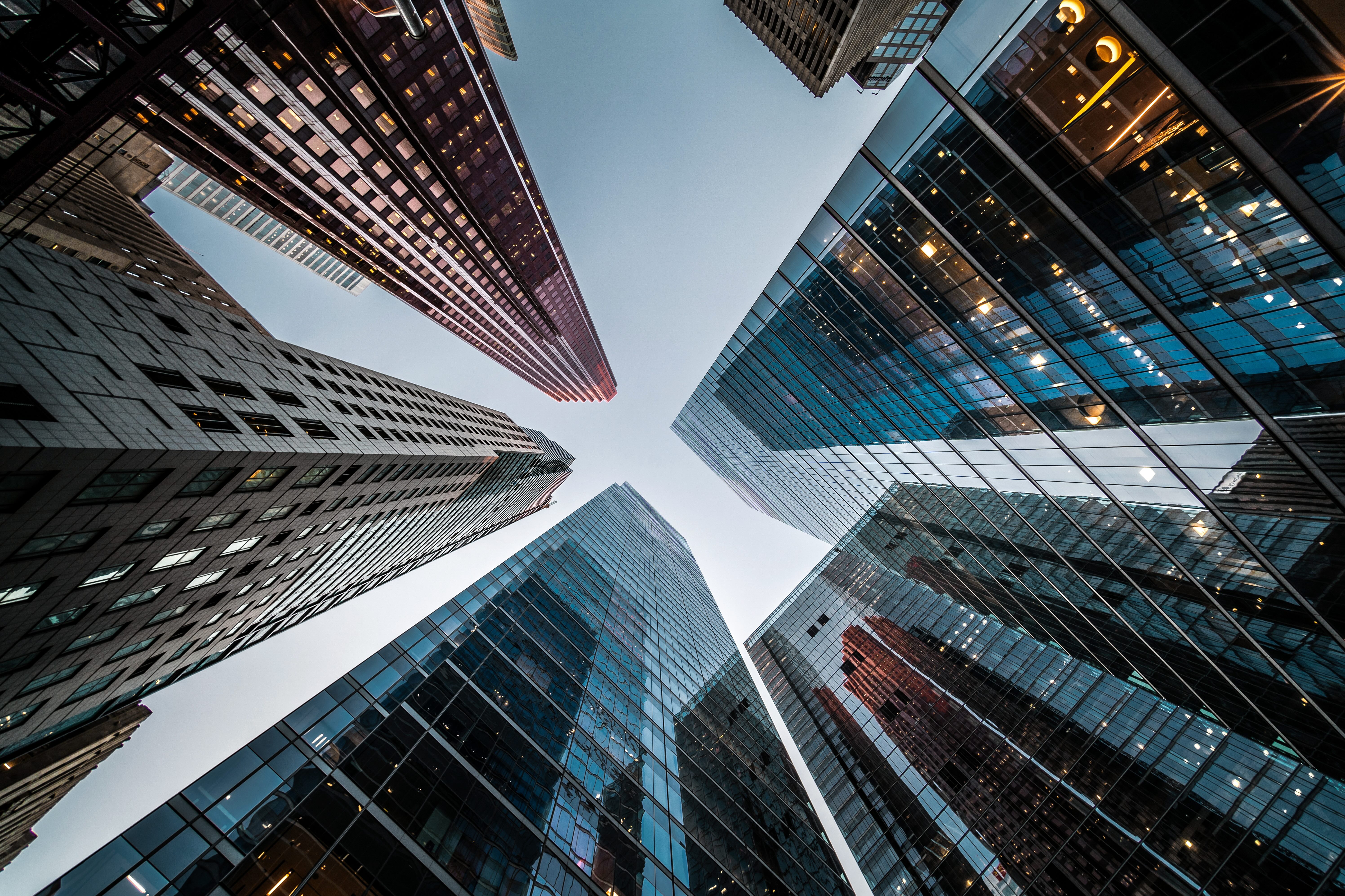 Upward view of tall skyscrapers with glass and steel exteriors against a clear sky.