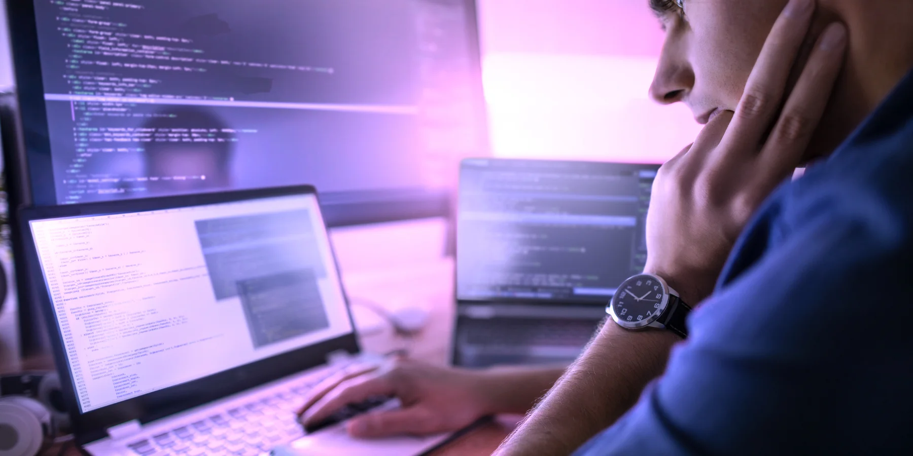 Entwickler arbeitet konzentriert an mehreren Bildschirmen mit Code und GitHub Workflow für Softwareentwicklung und KI gestützte Programmierung.