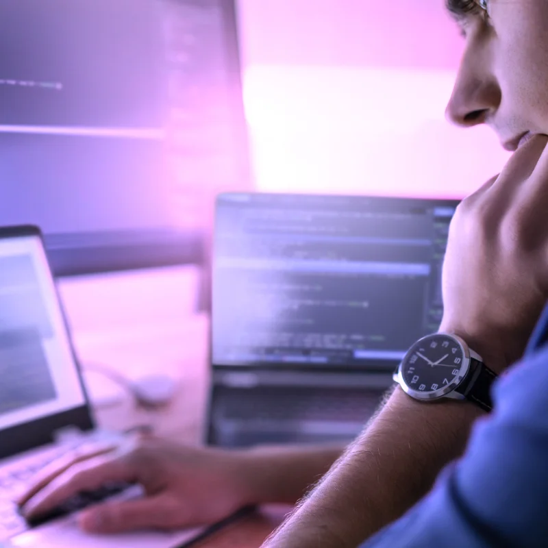 Entwickler arbeitet konzentriert an mehreren Bildschirmen mit Code und GitHub Workflow für Softwareentwicklung und KI gestützte Programmierung.