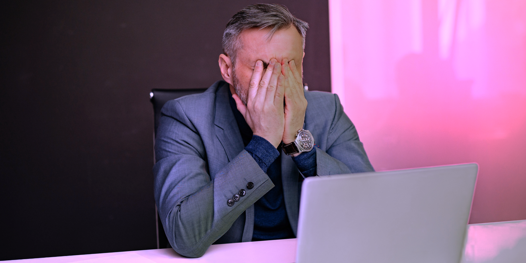 Geschäftsmann sitzt vor einem Laptop und bedeckt frustriert sein Gesicht bei der Auswertung einer KI-Sichtbarkeitsanalyse.