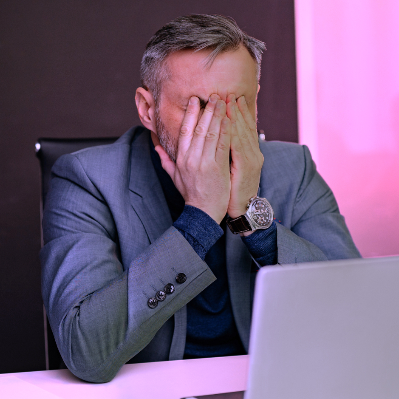 Geschäftsmann sitzt vor einem Laptop und bedeckt frustriert sein Gesicht bei der Auswertung einer KI-Sichtbarkeitsanalyse.