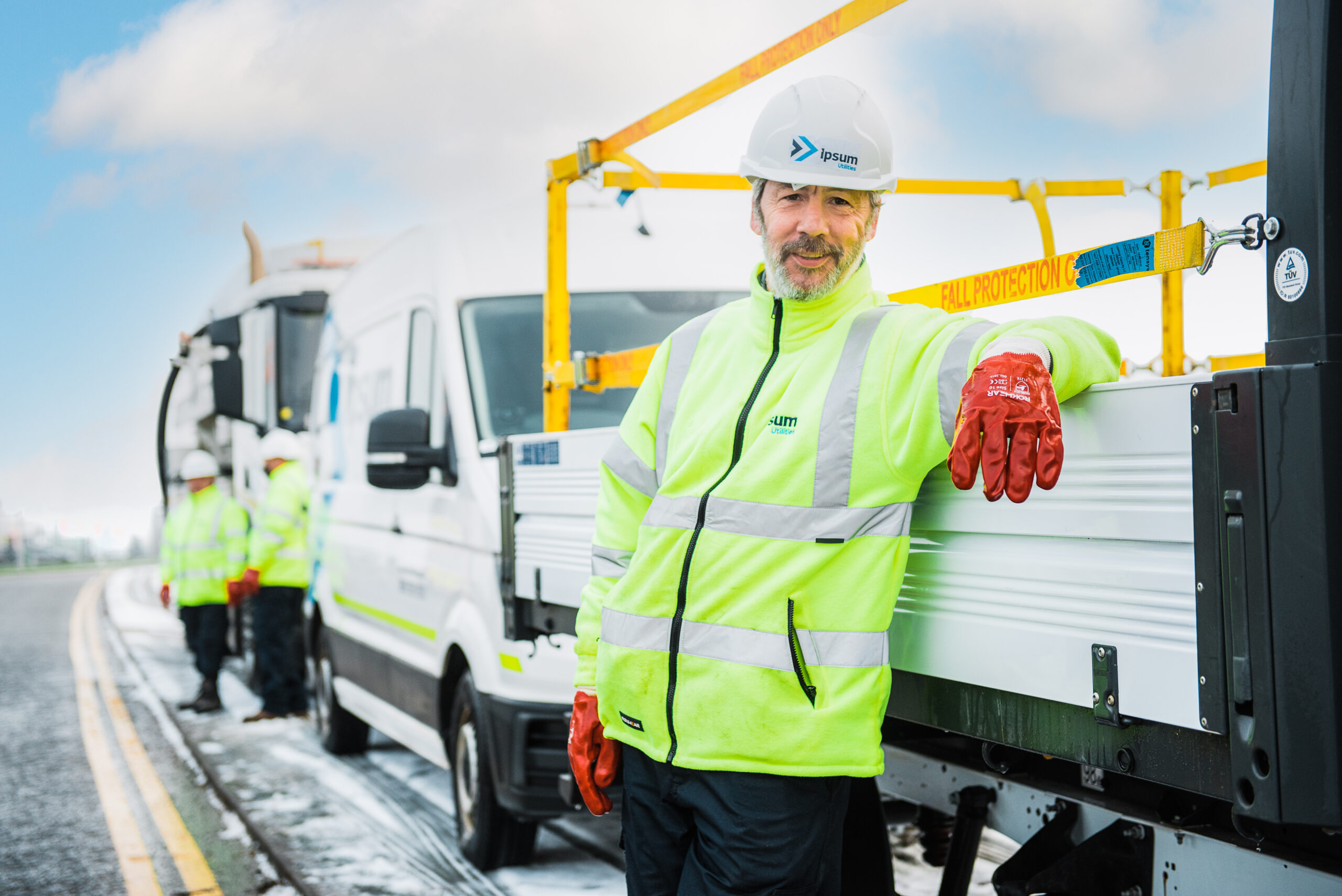 Worker in high-visibility jacket and hard hat leaning on utility truck with fall protection equipment.