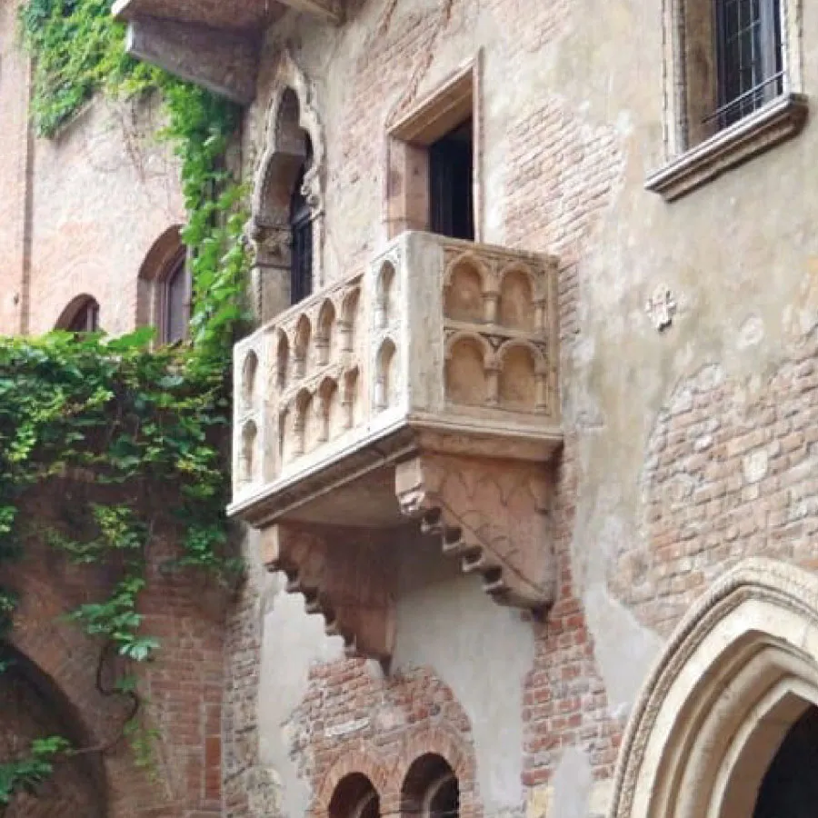 Stone balcony with ornate arches on an old brick building with ivy growing on the walls.