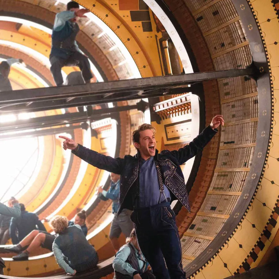 Joyful man in patterned jacket posing in front of a spiraling architectural structure with multiple reflections.