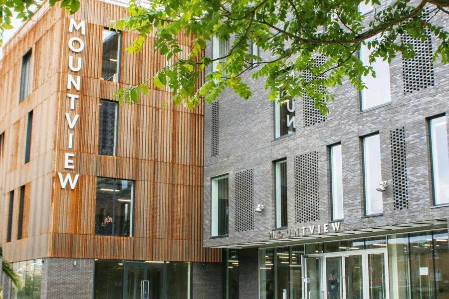 Modern building exterior with 'MOUNTVIEW' signage, featuring wood and brick facades and green tree branches overhead.