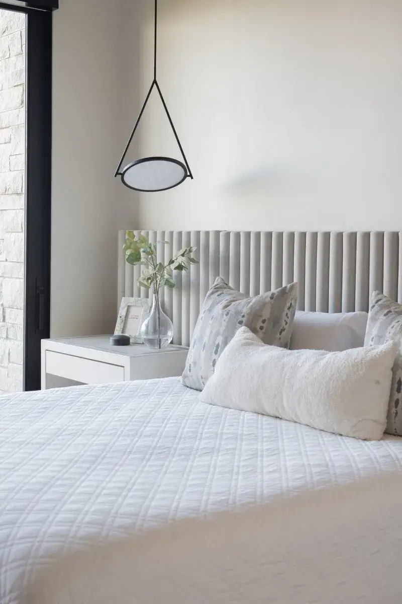 Modern bedroom with white quilted bed, patterned pillows, vertical grey headboard, and hanging lamp.