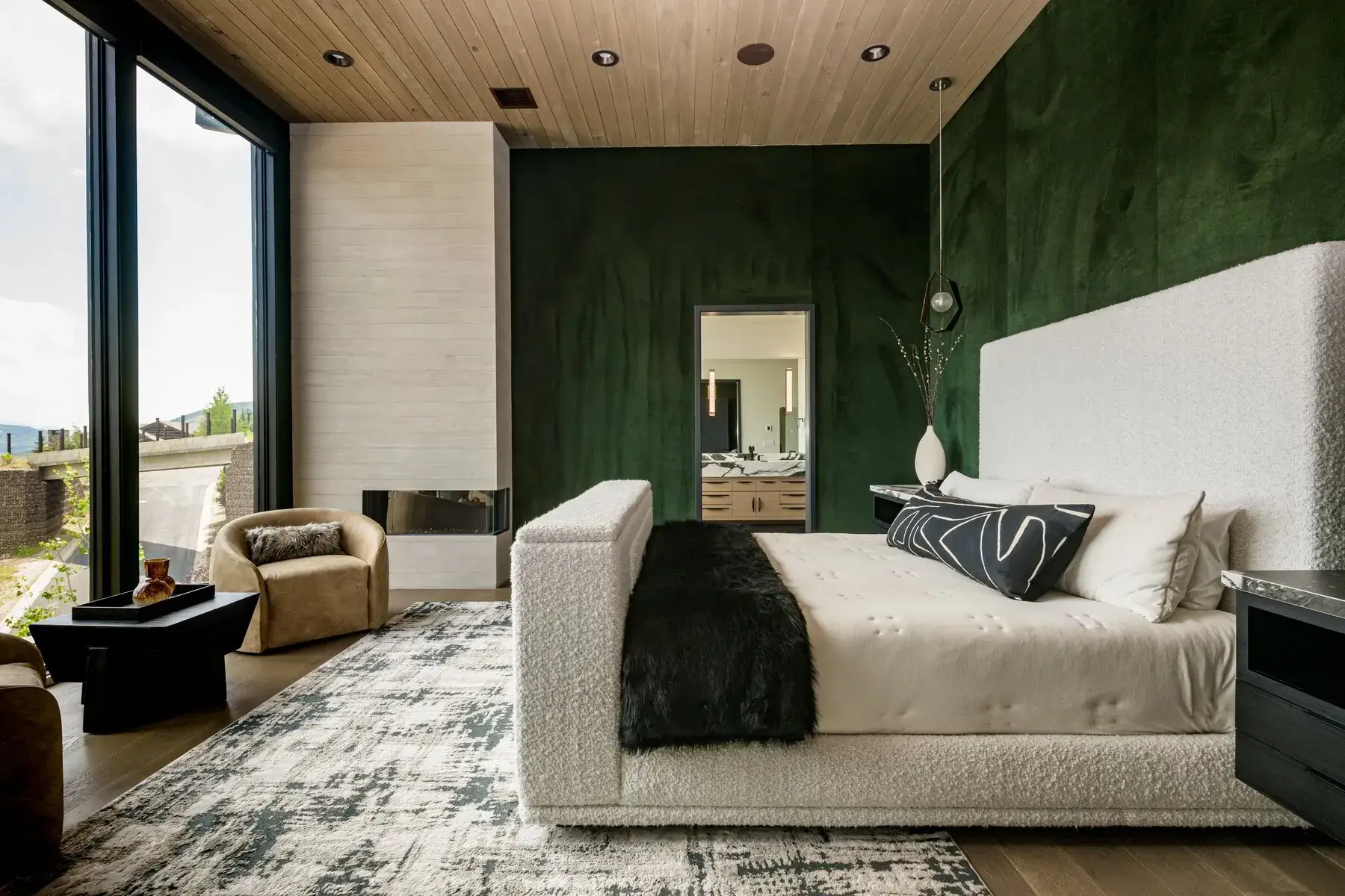 Modern bedroom with white upholstered bed, black throw, green accent wall, and large window view.
