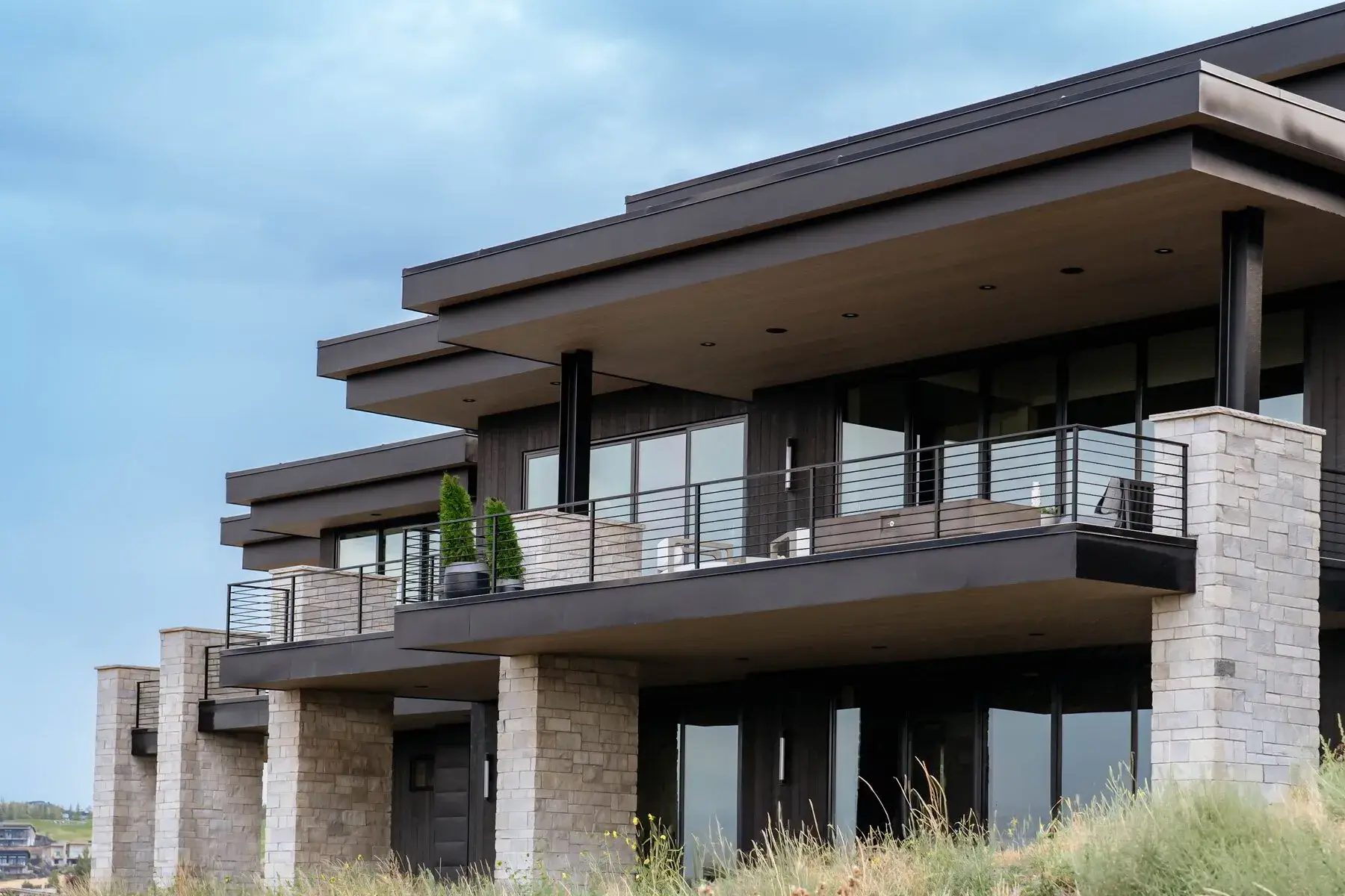 Modern stone and wood building with large balconies and glass doors under a cloudy sky.