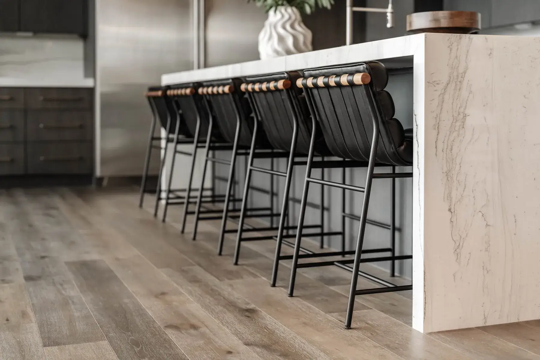 Row of black cushioned bar stools with wood accents at a white marble kitchen island.
