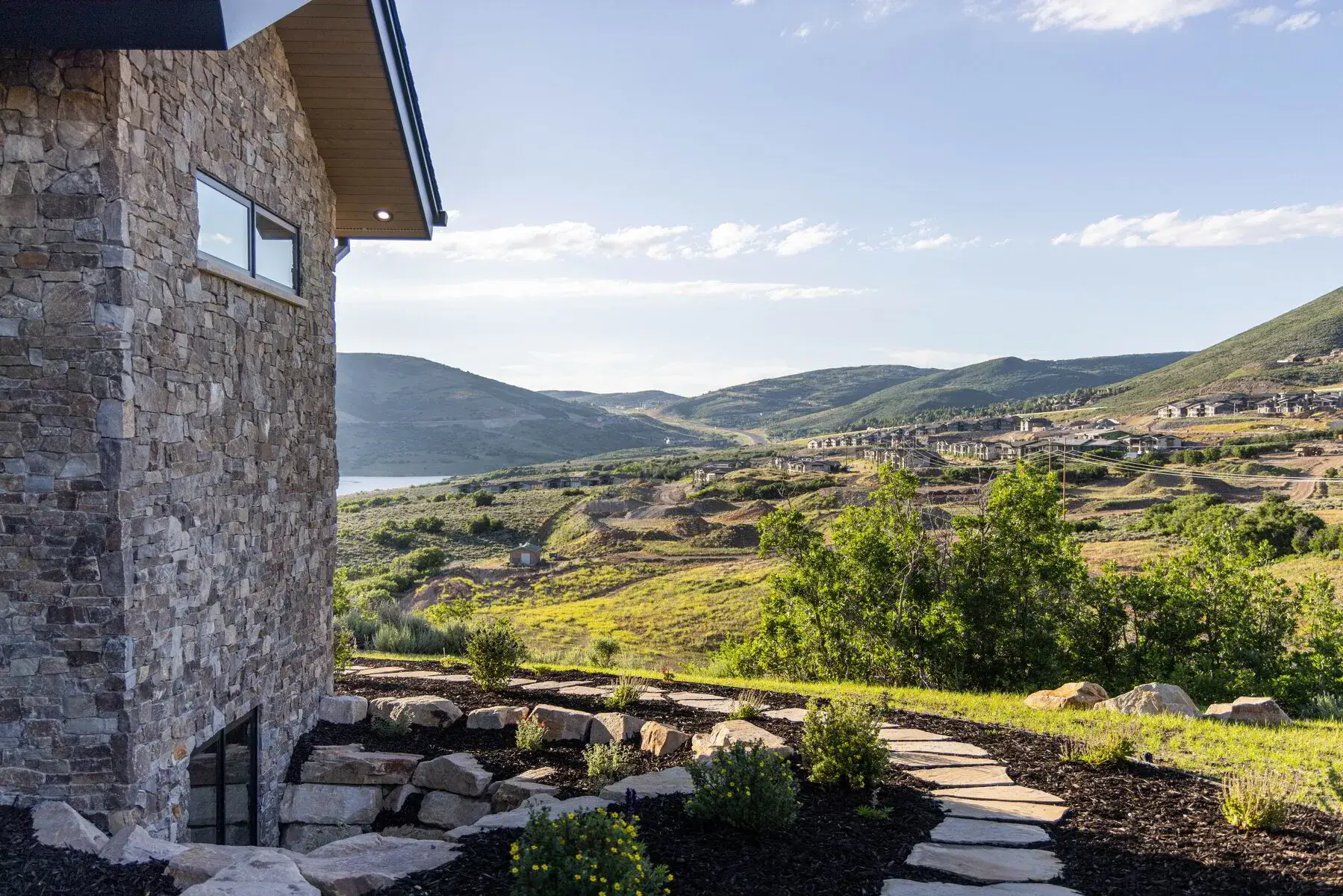 Stone house wall with window beside a stone path leading to green hills and a partly cloudy sky.
