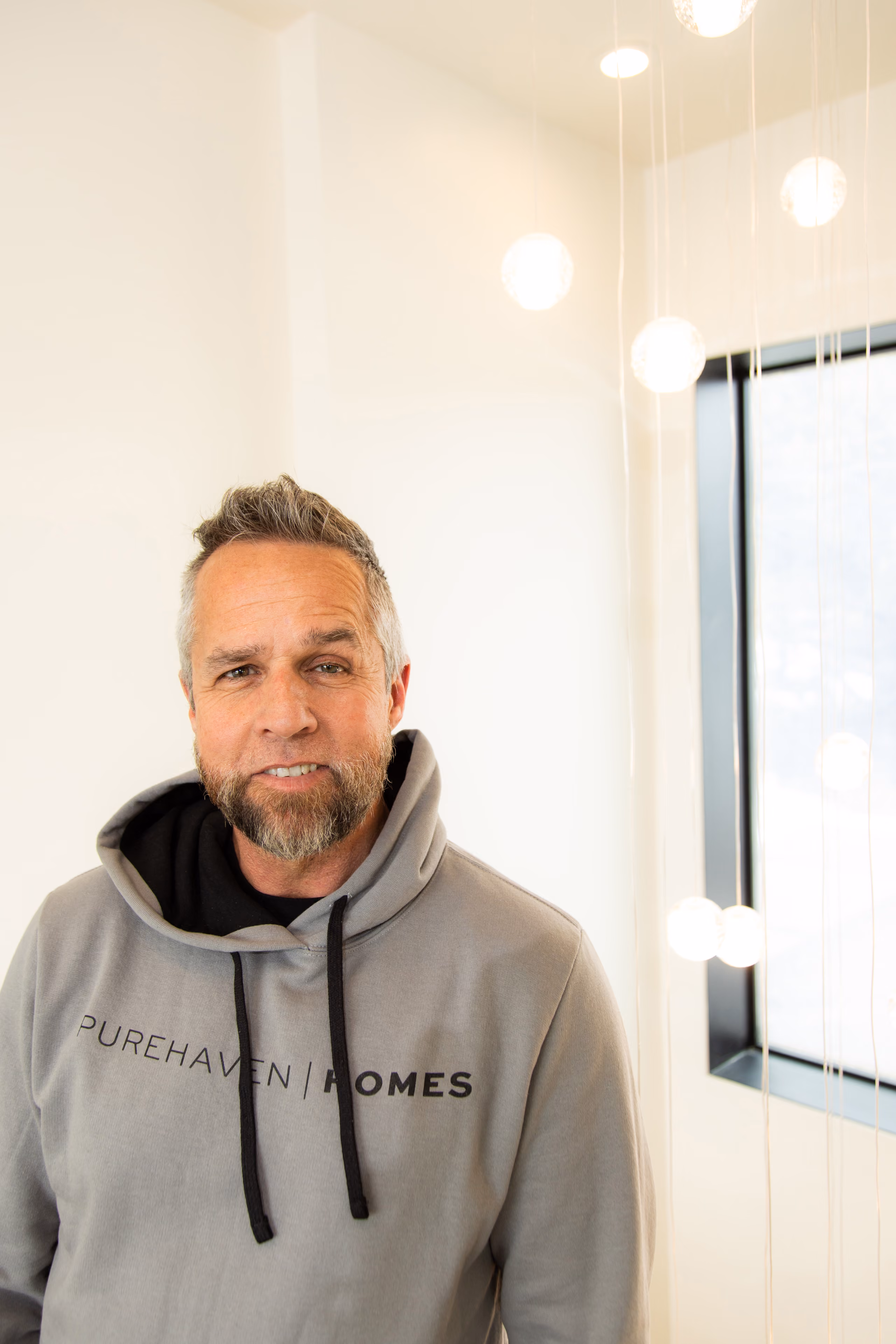 Smiling man with gray beard wearing a gray hoodie that says PUREHAVEN HOMES.