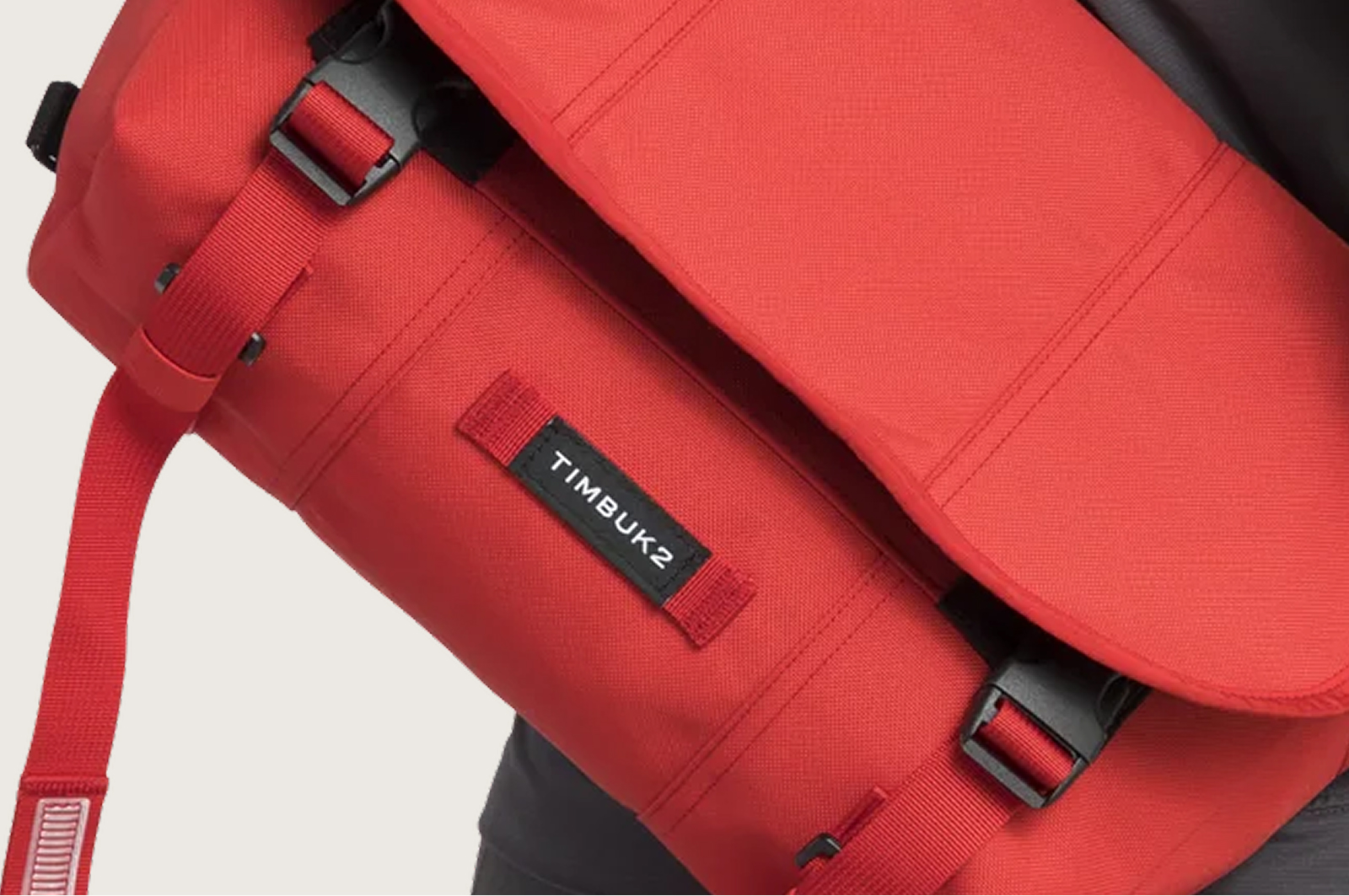 Close-up of a red Timbuk2 messenger bag showing black buckle closures and the Timbuk2 logo on the front flap.